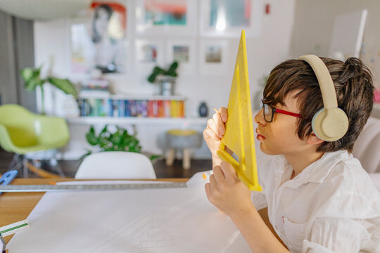 Boy wearing headphone looking through triangle tool ruler