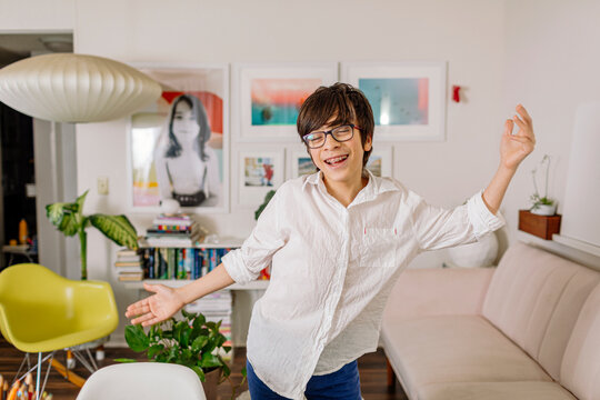 Happy Pre-teen with braces dancing in colorful room by bookshelves and wall gallery