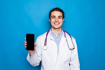 Male on-line doctor man show screen on mobile phone isolated on blue background. Epidemic pandemic...
