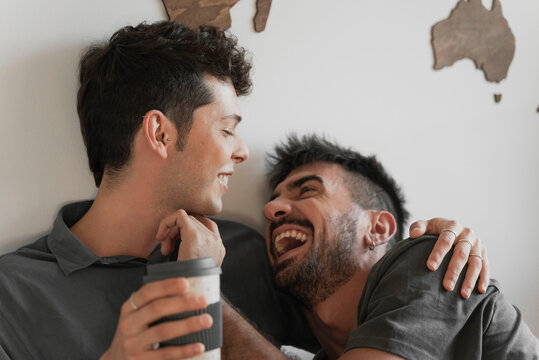 Same sex couple hugging in the room drinking coffee. 