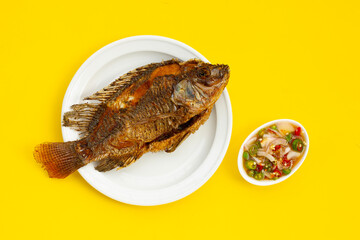 Fried fish in white plate on yellow background.