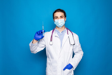 Portrait of a smiling young male doctor with stethoscope dressed in uniform standing and holding a syringe over white background