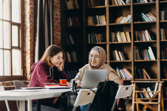 Positive diverse students studying in library with laptop