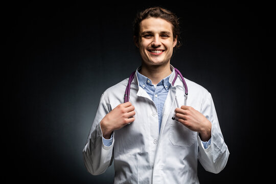 Handsome doctor with stethoscope in hand on black background.