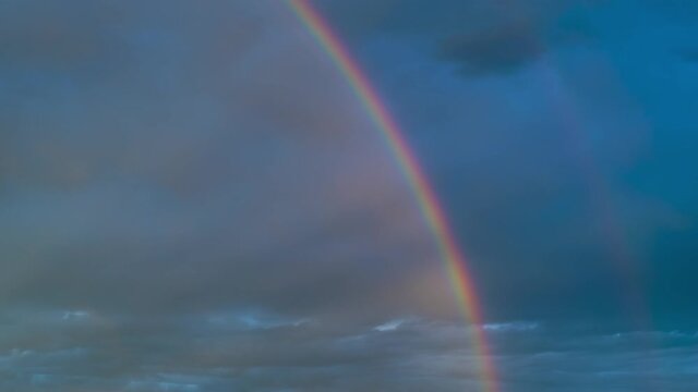 Time lapse of intense double rainbow on dark blue sky after rain. Timelapse,  light rays, copy space.