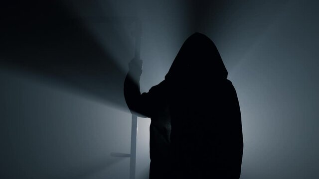 Silhouette scytheman frightening indoors. Grim reaper holding scythe in darkness
