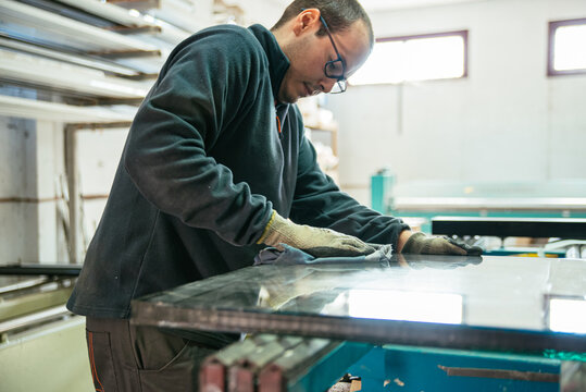 Busy man cleaning glass of window at factory