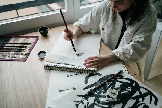 Young woman writing japanese kanji characters with a brush and ink