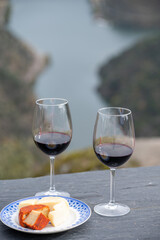 Tasting of Portuguese red dry wine, produced in Douro Valley with goat and sheep cheese and Douro river and terraced vineyards on background in autumn, Portugal