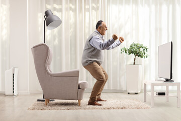 Mature man cheering in front of a tv at home