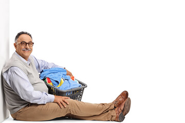 Smiling mature man sitting and holding a laundry basket