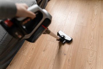 Cleaning wooden floor with wireless vacuum cleaner. Handheld cordless cleaner. Household appliance....