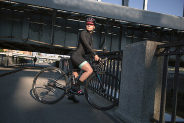 Portrait of female cyclist wearing helmet and goggles illuminated by the sun during morning workout on the waterfront in the city. Rest after training.