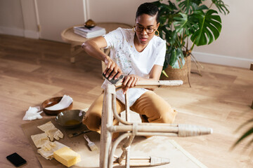 Black craftswoman sanding bamboo table on floor