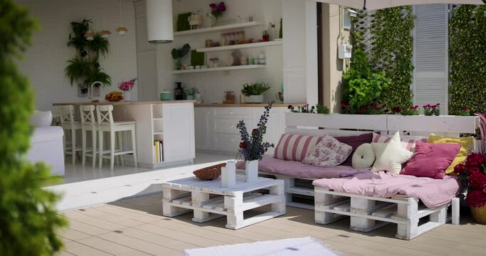 a lounge zone hand crafted from wooden pallets on open space patio with kitchen and living room, cozy rooftop apartment