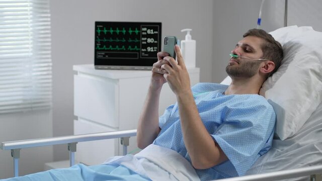 Man in hospital with the mobile phone and earphones lying alone in bed. Male Patient Using Mobile Phone In Hospital Bed