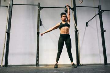 Muscular Hispanic sportswoman lifting kettlebell over head 