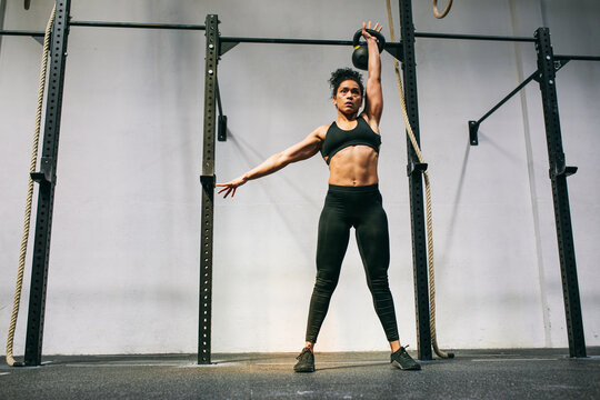 Muscular Hispanic sportswoman lifting kettlebell over head 