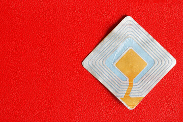 RFID tag transponder on a red background. A concept for the use of wireless RFID technologies in...