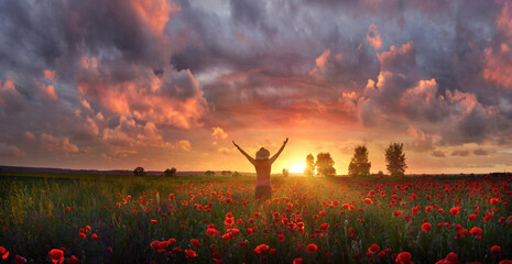 Joyful woman feels delight among poppies at summer sunset