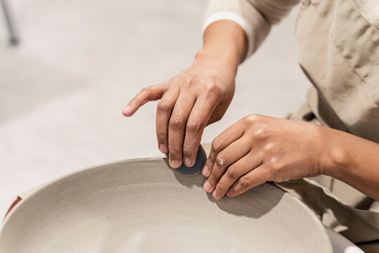 Female artisan sitting at the desk in the pottery workshop and working on a clay bowl.