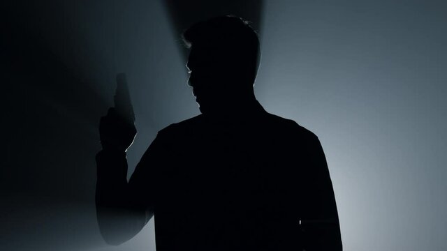 Silhouette gunner raising hand with pistol in darkness. Criminal holding gun.