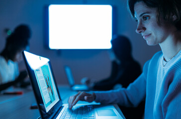 Smiling woman typing on laptop in dark office at night