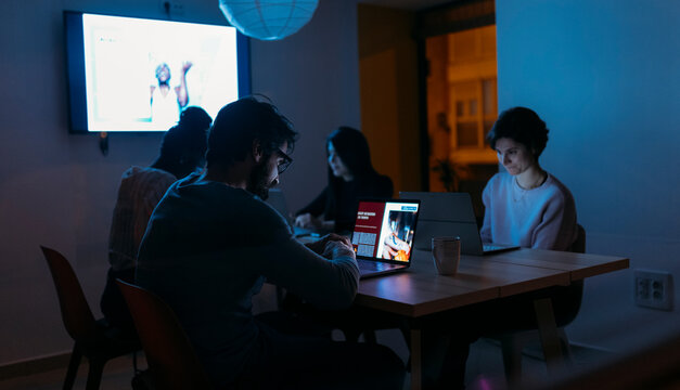 Group of diverse colleagues gathering at table in modern workspace at night