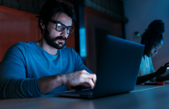 Serious man working on laptop in office with diverse colleagues