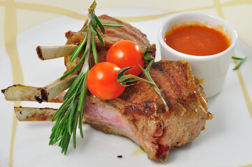 Rack of lamb, with tomatoes red pepper and rosemary on white plate closeup