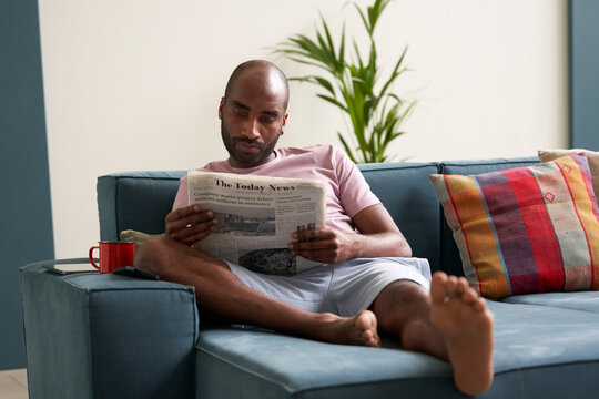 Afro American male relaxing at sofa with newspaper.