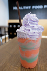 Cup of unicorn smoothie. rainbow ice cream mixed with blueberry syrup topped with whipping cream.