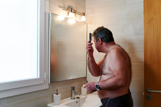 Mature Man Combing His Hair In A Bathroom Mirror