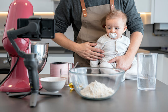 Father with a baby sitting on a kitchen table full of cooking utensils and a mobile