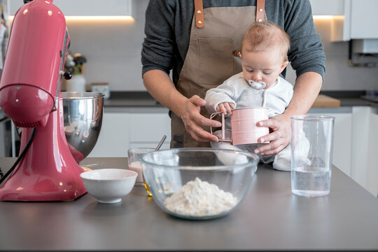 Baby sitting at kitchen table clutching a cup next to an adult
