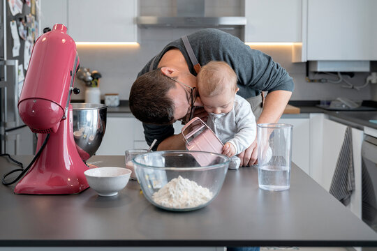 Father kissing baby sitting at kitchen table