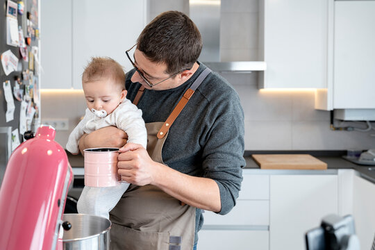 Man holding a baby while showing him a cup in a kitchen