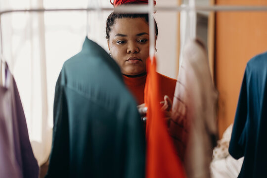 Focused black woman picking clothes from hangers at home