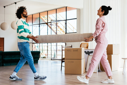 Multiracial couple carrying carpet in new flat