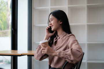 At a cafe shop, a young gorgeous woman is on the phone with a cup of coffee. conversing and setting up appointments for her customer.