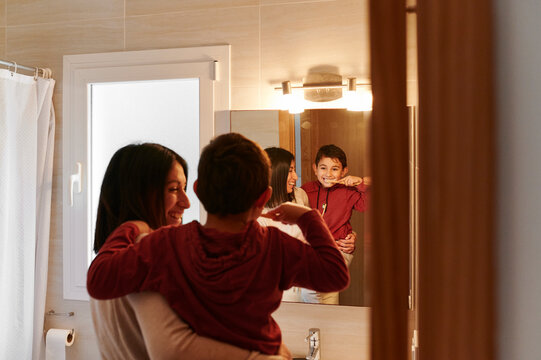 Laughing mom watching her son brush his teeth