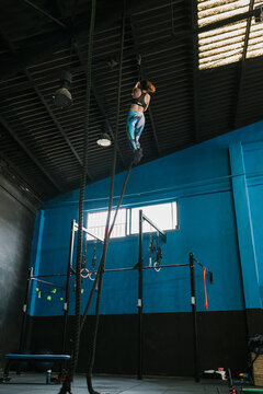 Unrecognizable sportswoman climbing rope in sports club