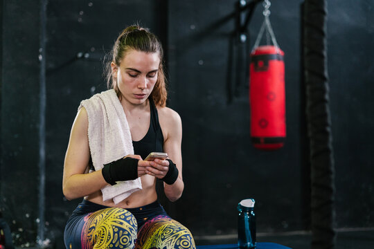 Sportswoman in boxing bandages using smartphone in gym