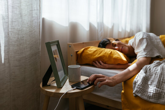 Tired woman turning off alarm on smartphone in morning