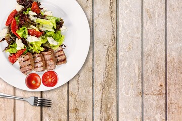 White plate of chicken salad with vegetables on a wooden table