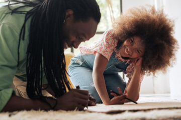Mixed race girl and her black father painting a banner in the floor while she is smiling and looking at camera