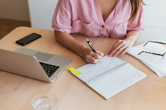Crop woman making notes near laptop