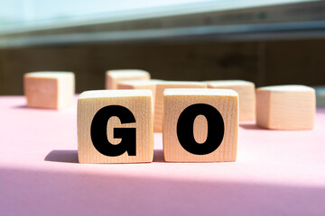 " go " text made of wooden cube on pink background.