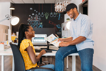 Happy black colleagues discussing project at table with laptop