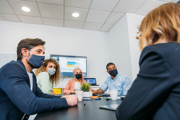 Crop multiethnic coworkers in cloth face masks speaking in office